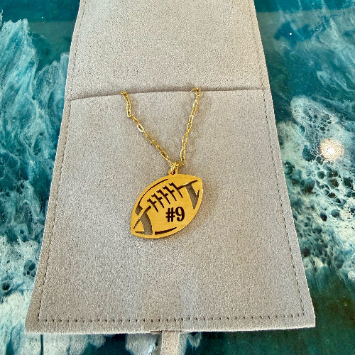 Gold necklace with a football-shaped pendant on a beige cushion against a textured blue background