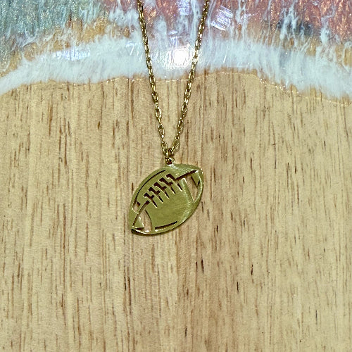 Gold necklace with a football-shaped pendant on a wooden surface