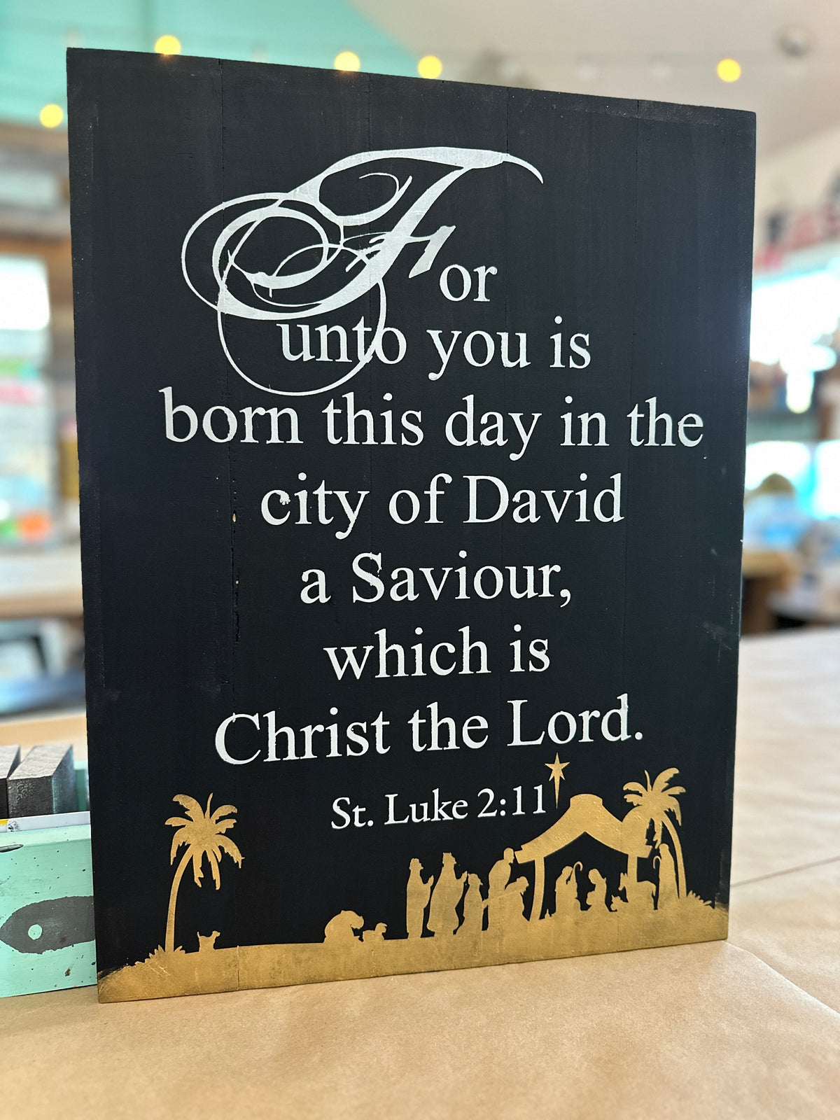 A decorative plaque with a Bible verse about the birth of Christ in the city of David, in black and gold colors.