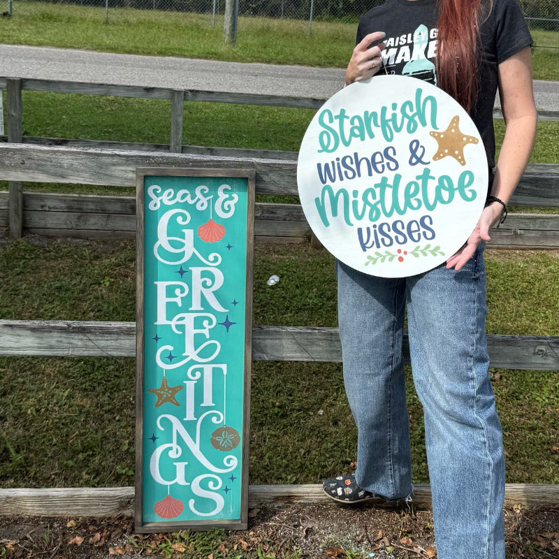 Person holding a decorative sign outdoors near a wooden fence and grassy area.