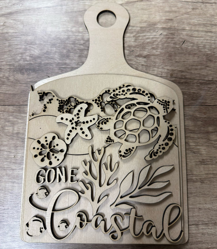 Wooden cutting board with coastal designs and text on a wooden surface