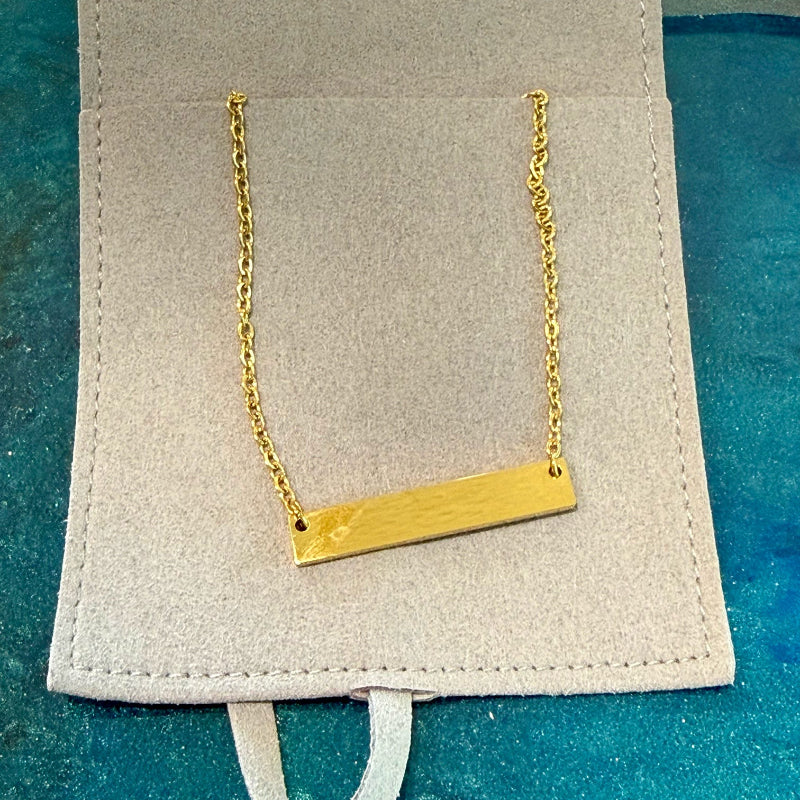 Gold necklace with a bar pendant on a beige card against a blue background