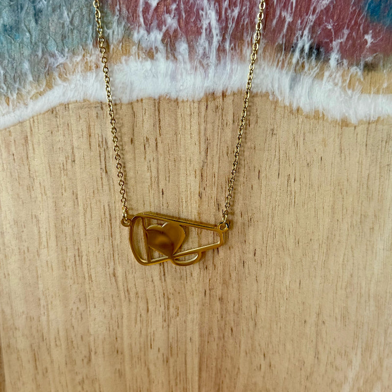 Gold necklace with a leaf pendant on a wooden surface with a water edge background