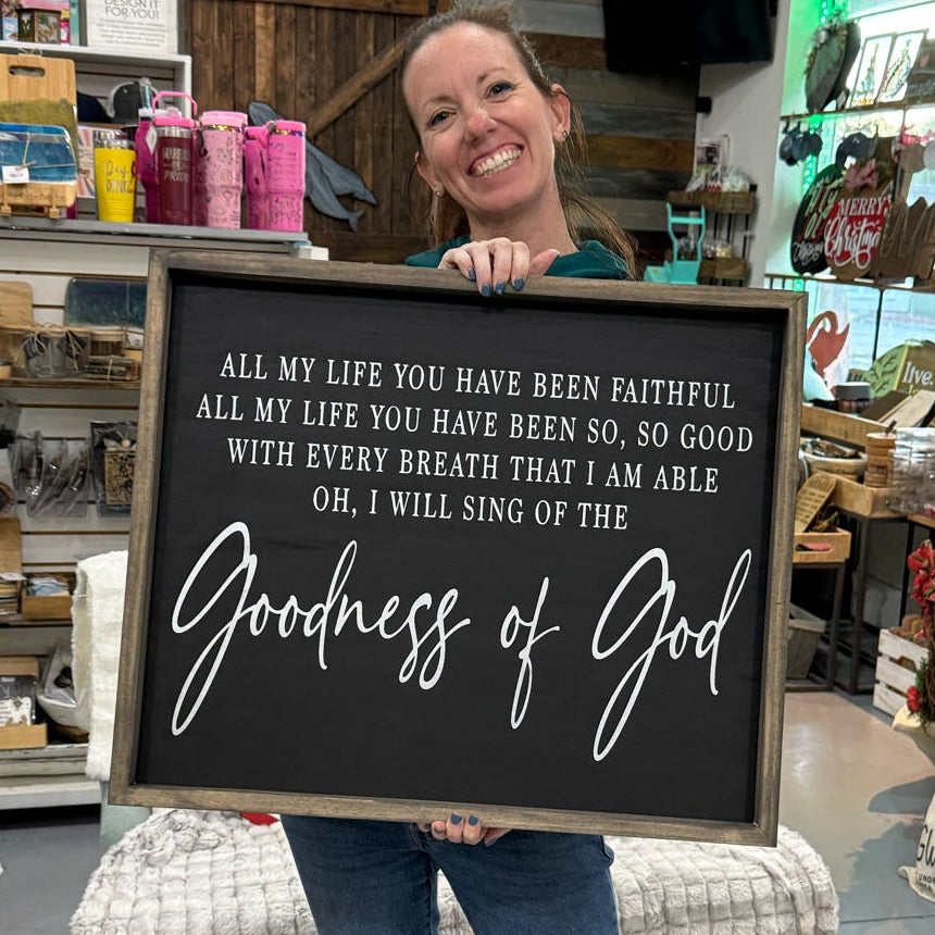 Person holding a sign with 'Goodness of God' in a store setting