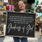 Person holding a sign with 'Goodness of God' in a store setting