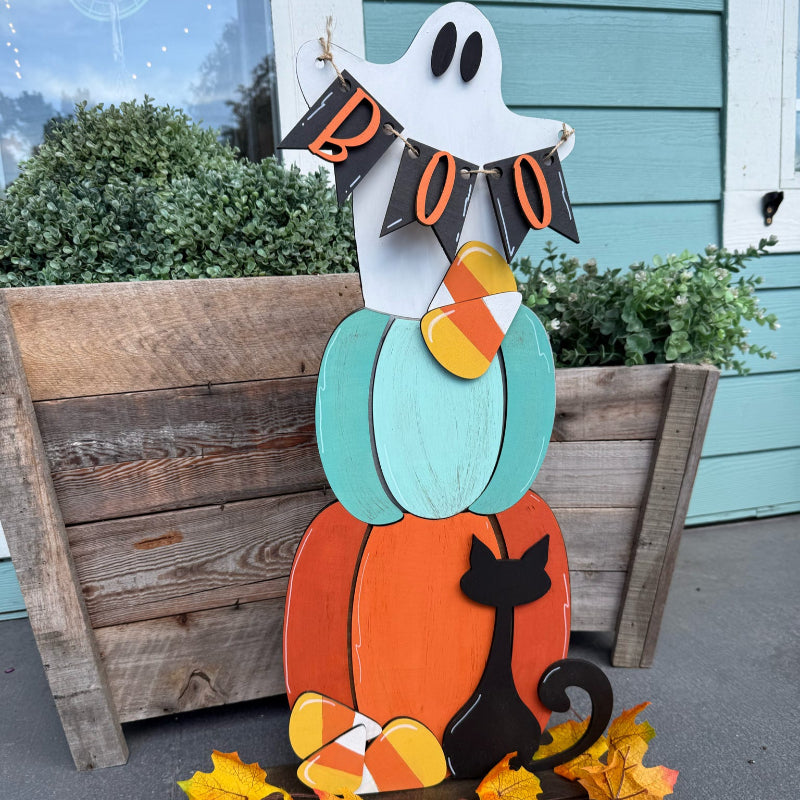 Halloween-themed decorative stand with ghost, pumpkin, and cat on a porch.