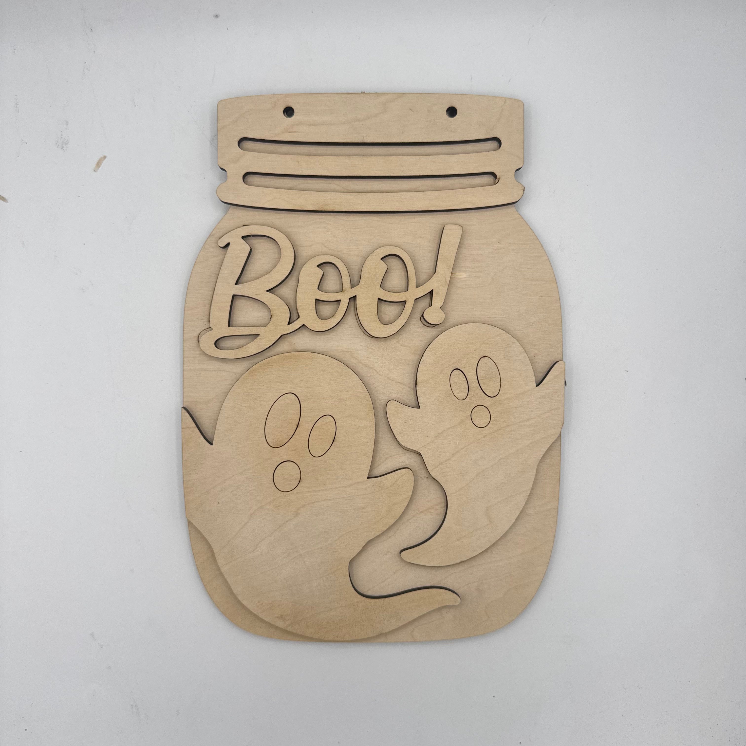 Unpainted wooden Halloween wall decor shaped like a mason jar with laser-cut ghosts and the word 'Boo!' on a light gray background.