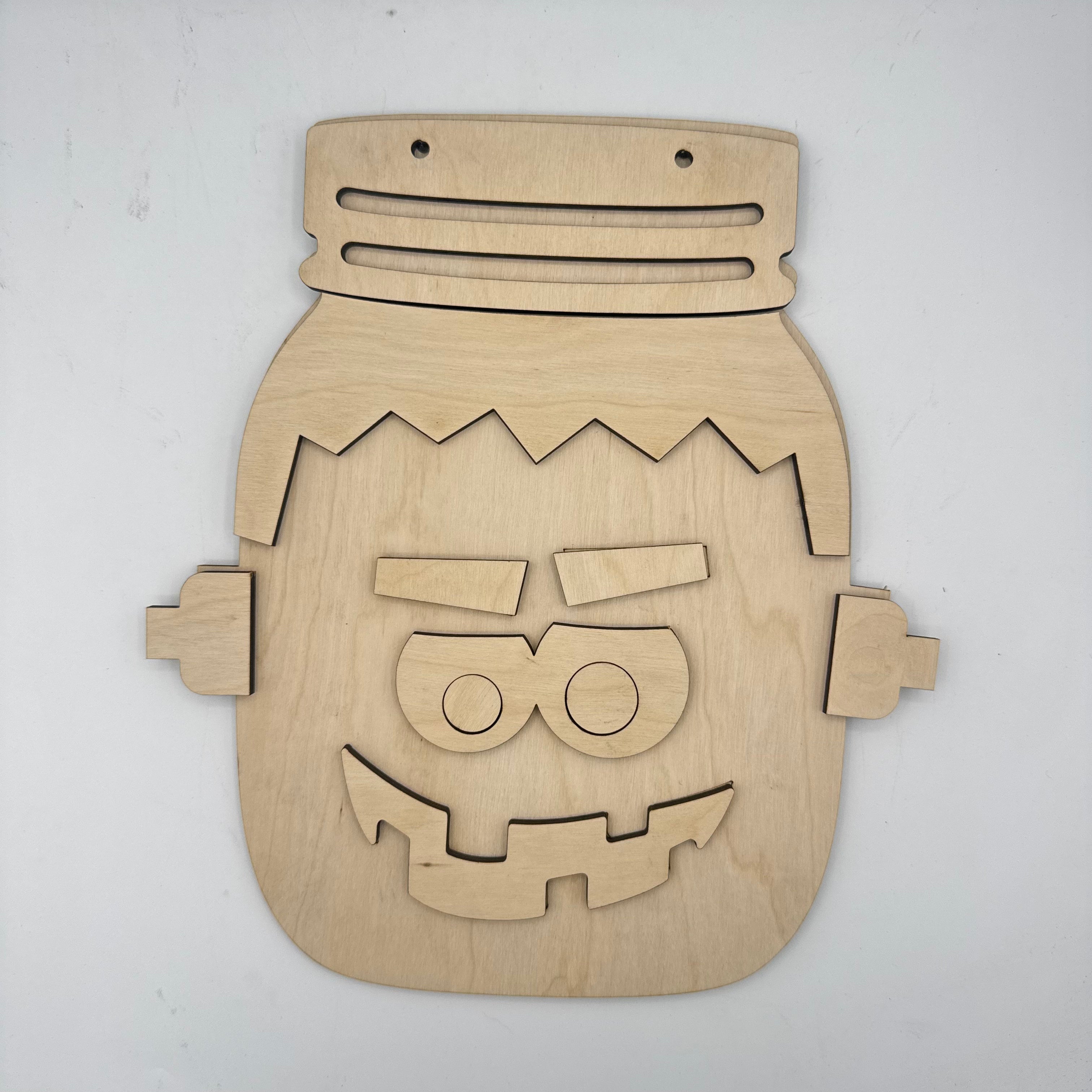 A wooden jigsaw puzzle shaped like a Frankenstein's monster head, made from light natural wood with laser-cut pieces, displayed on a plain off-white background.