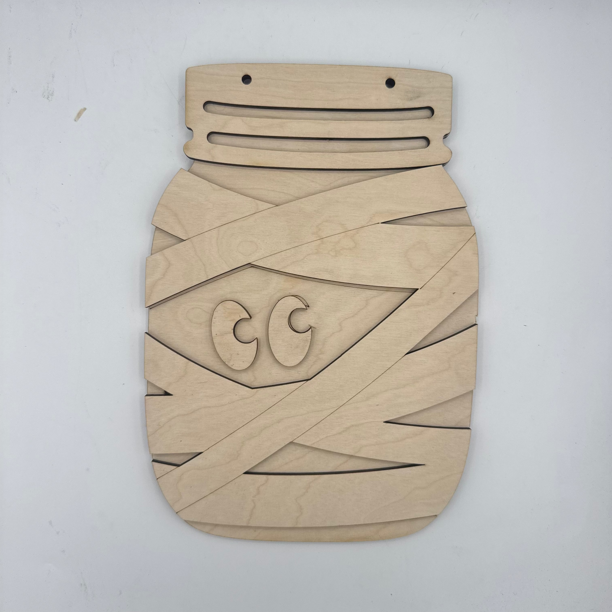 A light natural wood decorative plaque or board with geometric cutout patterns and a stylized face design, photographed against a plain white background.