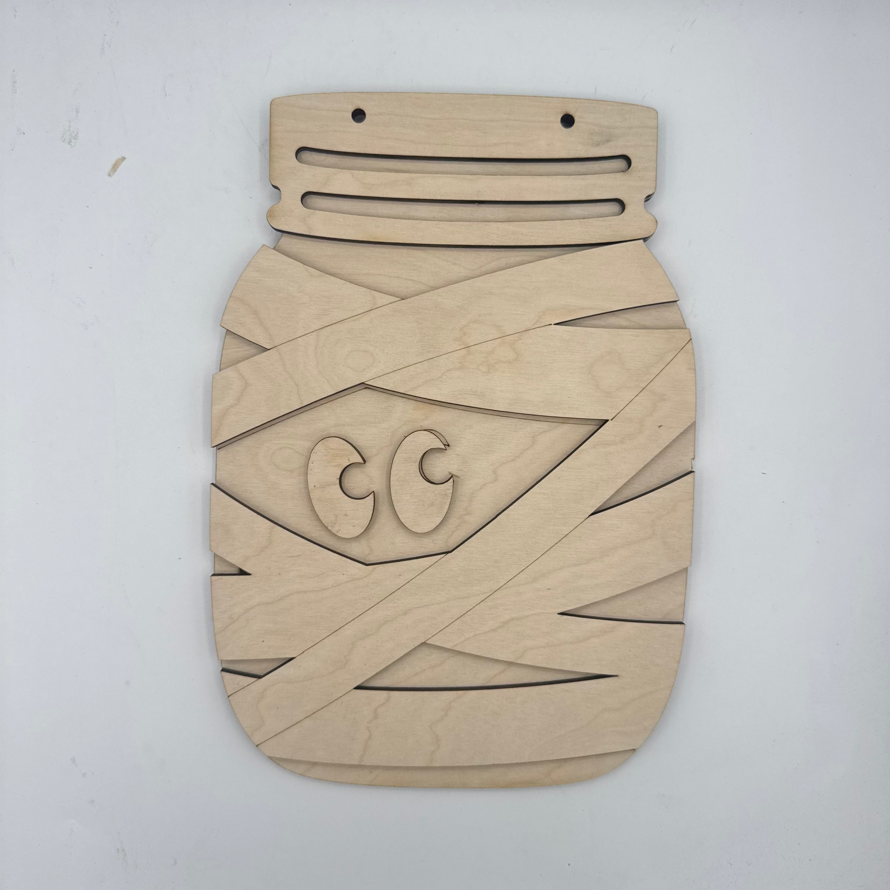 A light natural wood decorative plaque or board with geometric cutout patterns and a stylized face design, photographed against a plain white background.