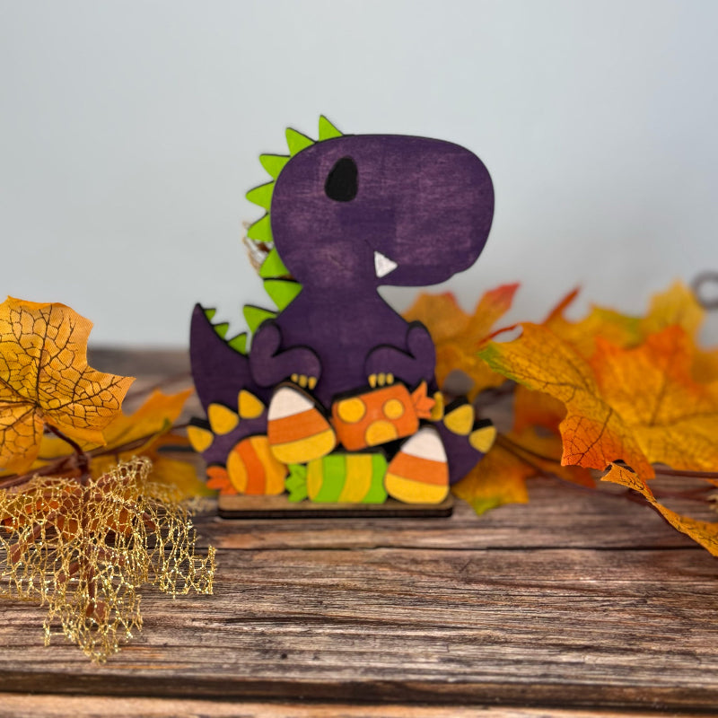 Wooden dinosaur figurine with candy corn design on a wooden surface with autumn leaves.