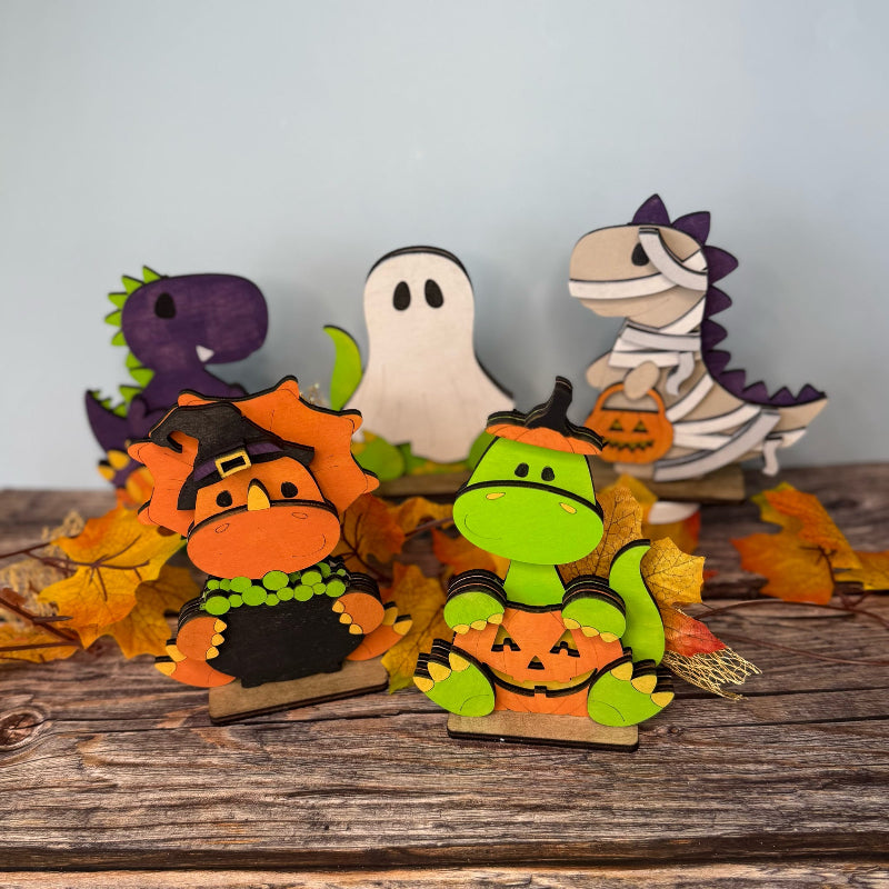 Halloween-themed dinosaur figurines on a wooden surface with autumn leaves.