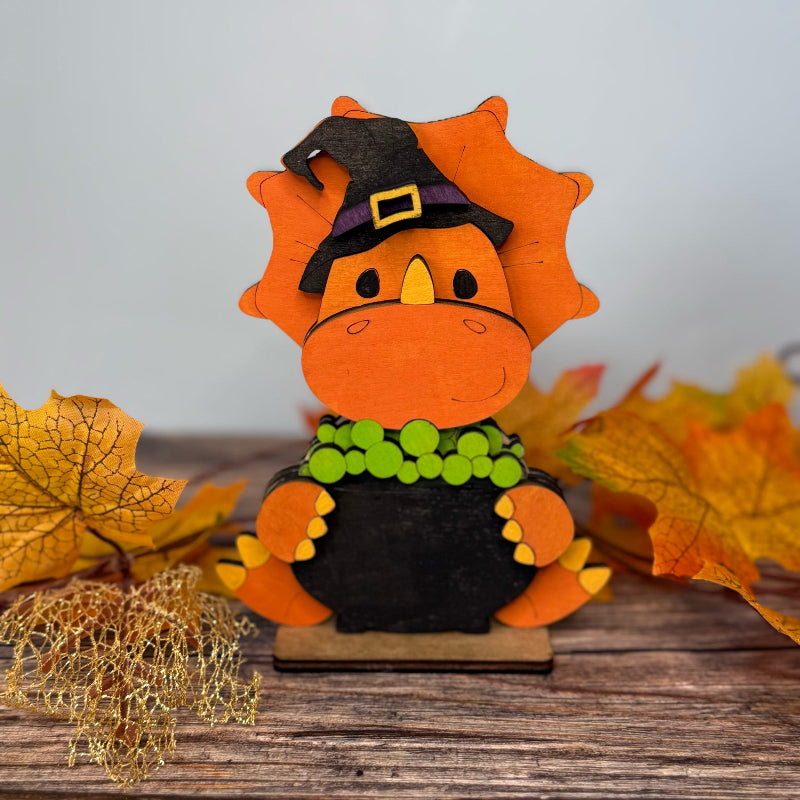 Decorative leaf figurine with a witch hat on a wooden surface with autumn leaves.