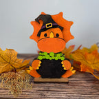Decorative leaf figurine with a witch hat on a wooden surface with autumn leaves.