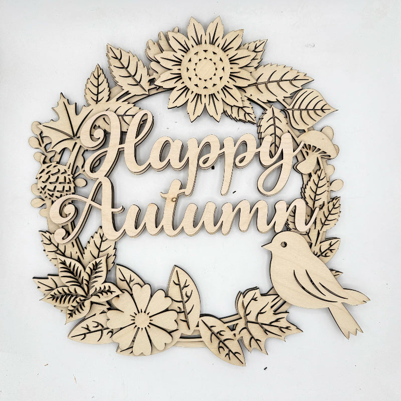 A laser-cut wooden decorative sign featuring the words 'Happy Autumn' in cursive script, surrounded by autumn leaves, flowers, a pinecone, and a small bird, shown on a plain white background.