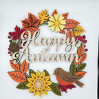 A decorative autumn wreath sign with the words “Happy Autumn” in light wood script, surrounded by layered fall leaves, sunflowers, berries, a pinecone, and a robin bird on a white background.