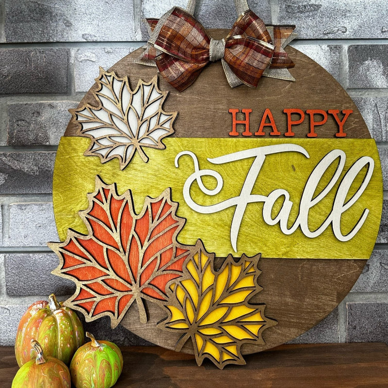 A round door hanger with a 'Happy Fall' text and 3D leaf designs in orange, yellow, and green colors, topped with a plaid bow.