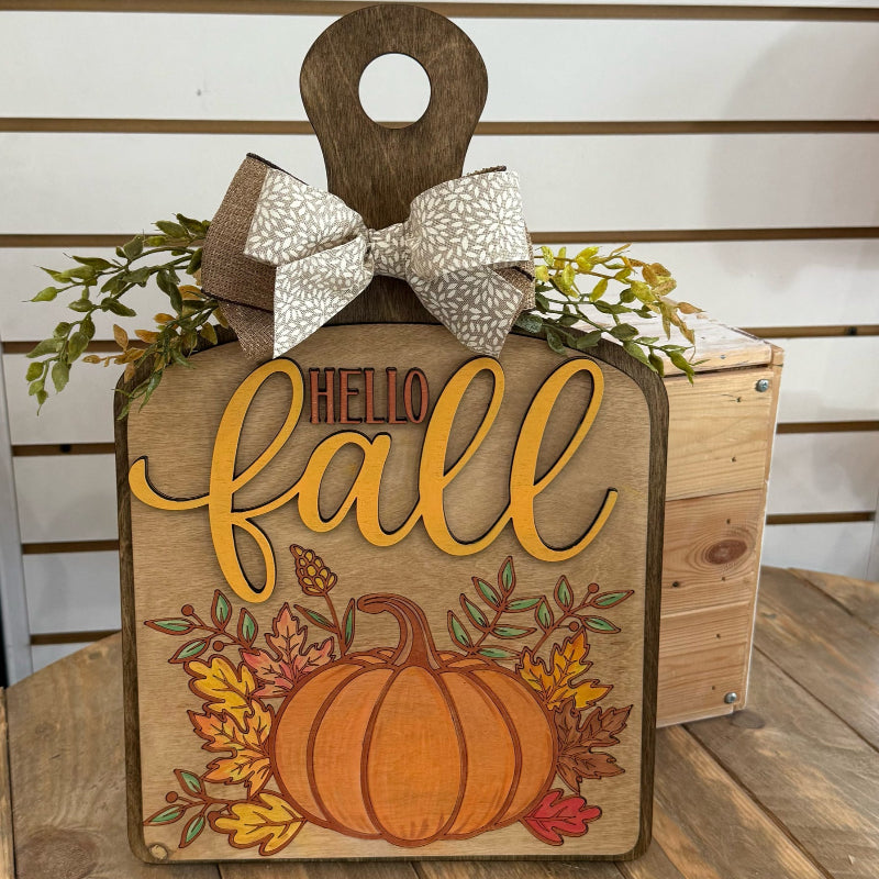 Wooden sign with 'Hello Fall' and pumpkin design, decorated with a bow and leaves.
