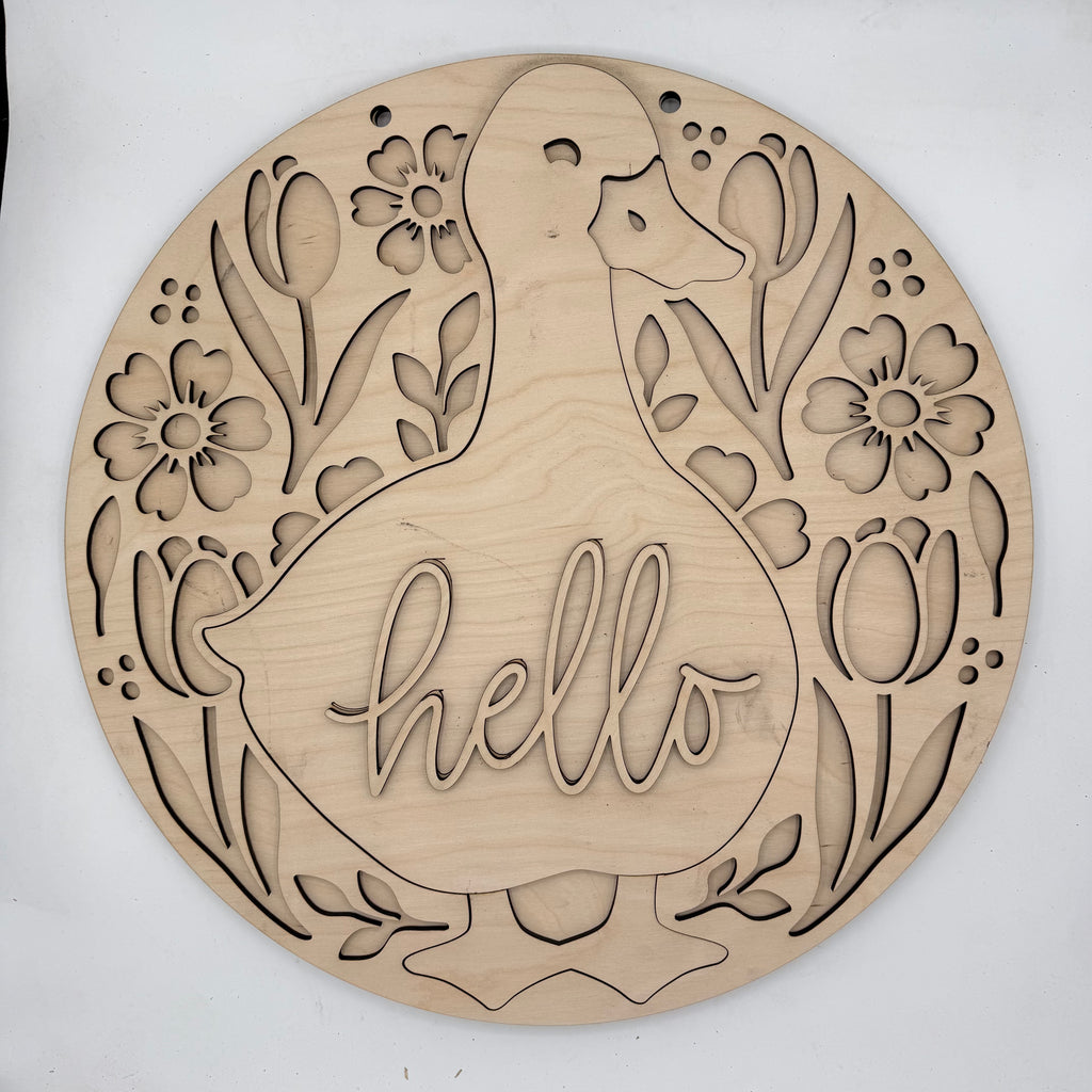 A round, laser-cut wooden wall sign featuring a duck silhouette with the word 'hello' cut into the center, surrounded by tulips and flowers. The natural wood grain is clearly visible against a plain white background.