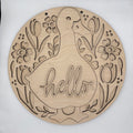 A round, laser-cut wooden wall sign featuring a duck silhouette with the word 'hello' cut into the center, surrounded by tulips and flowers. The natural wood grain is clearly visible against a plain white background.