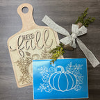 Wooden cutting board with 'Hello Fall' engraving, decorative ribbon, and pumpkin design card on a wooden surface.