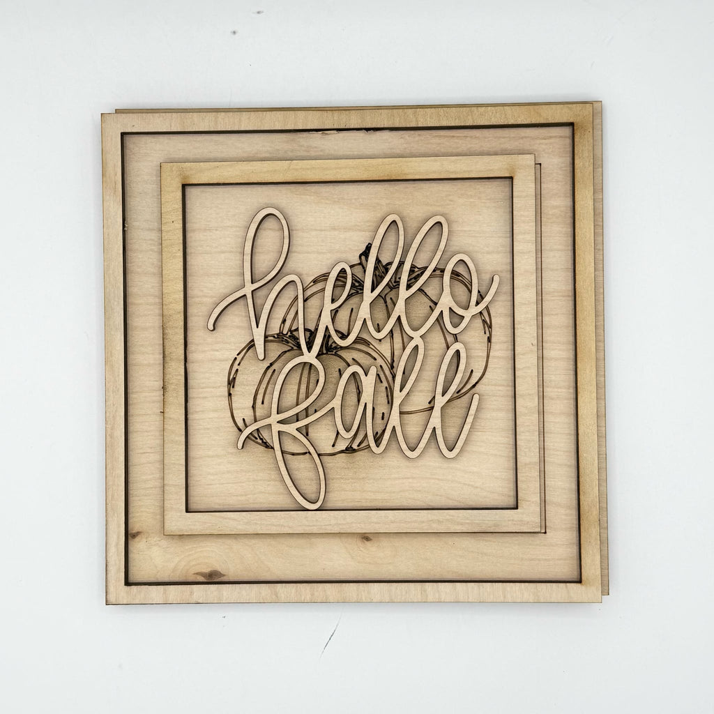 A square wooden wall sign with layered natural wood frames and laser-cut script reading 'hello fall' over a pumpkin outline, shown against a plain white background.