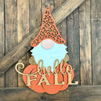 Decorative sign with a gnome face and 'Hello Fall' text on a wooden background