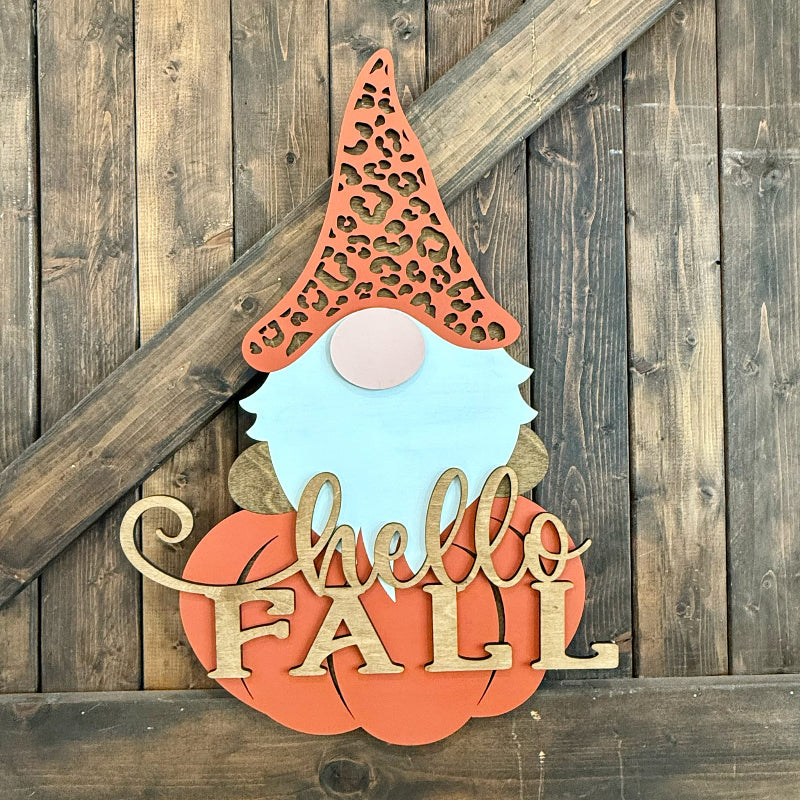 Decorative sign with a gnome face and 'Hello Fall' text on a wooden background