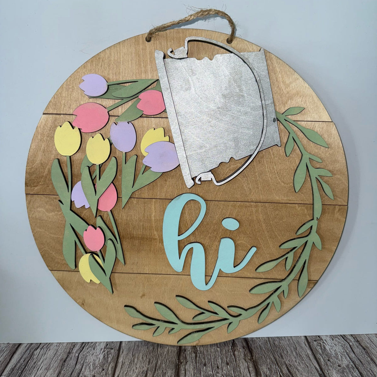 Wooden circular sign with floral design and 'hi' text on a light gray background