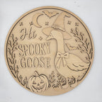 Round laser-cut wooden plaque featuring a carved goose wearing a witch hat, the phrase 'Hi SPOOKY GOOSE,' a jack-o'-lantern, bats, stars, and a crescent moon on a light wood background.