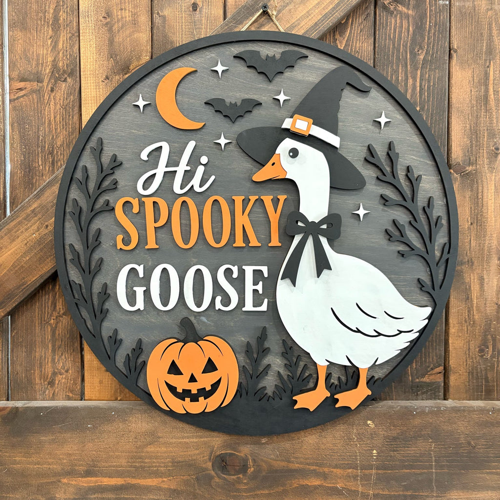 Round wooden Halloween wall sign featuring a white goose wearing a witch hat, orange text reading 'Hi SPOOKY GOOSE,' a jack-o'-lantern, bats, stars, and a crescent moon on a rustic wood plank background.