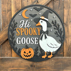 Round wooden Halloween wall sign featuring a white goose wearing a witch hat, orange text reading 'Hi SPOOKY GOOSE,' a jack-o'-lantern, bats, stars, and a crescent moon on a rustic wood plank background.