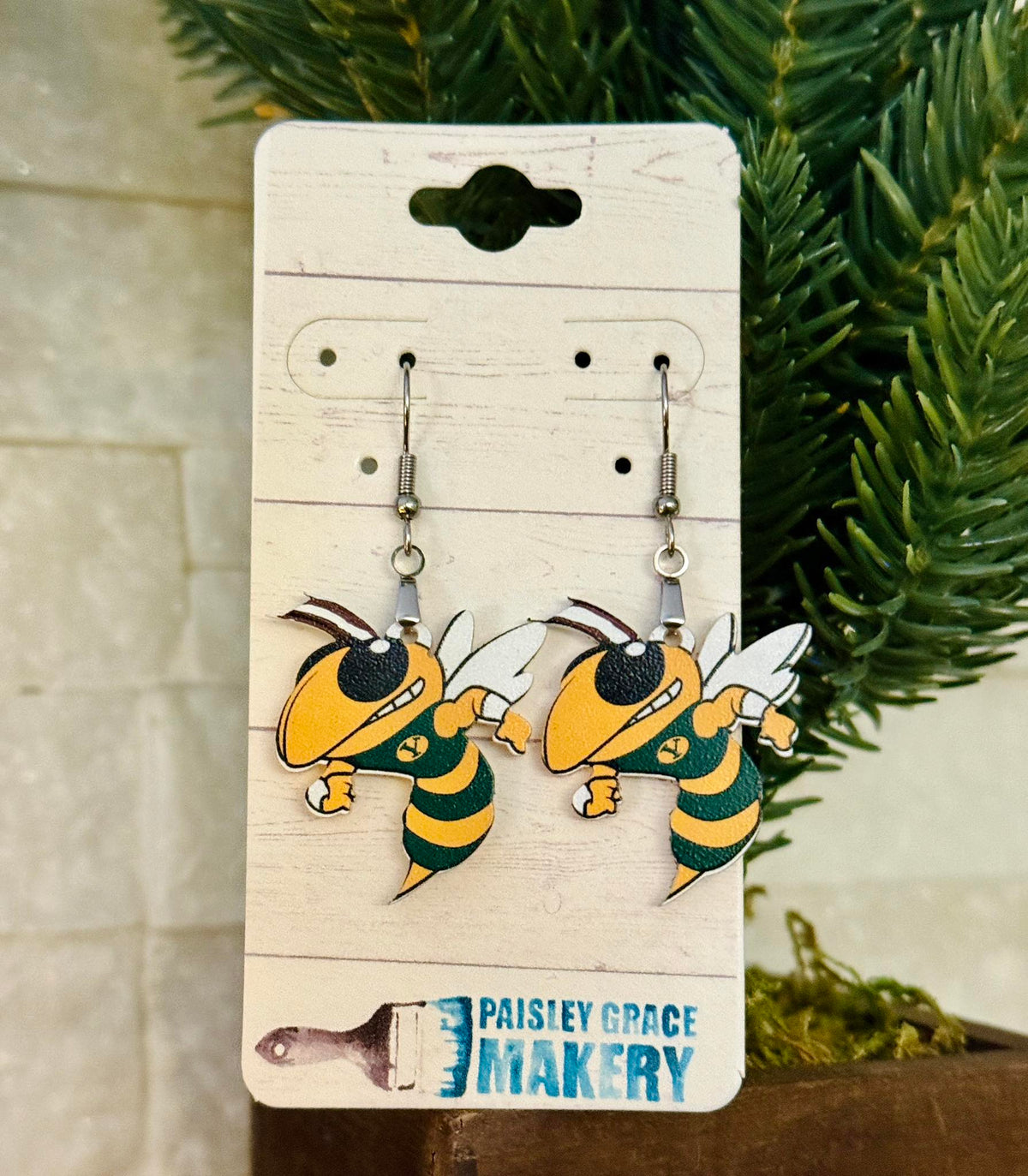 Pair of Hornet  bee-shaped earrings on a 'Paisley Grace Makery' branded card with green foliage in the background. Yulee Hornets.