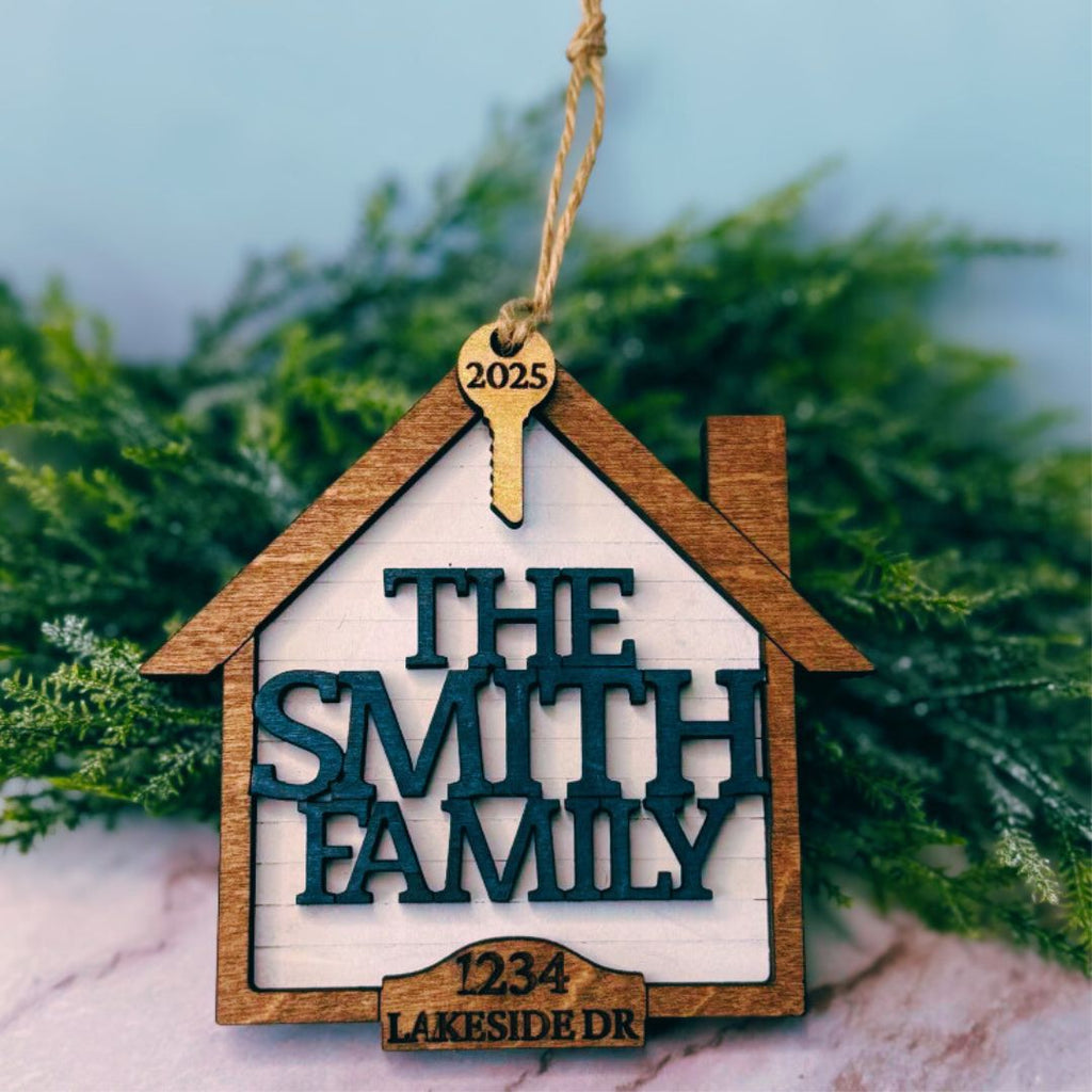Decorative house-shaped ornament with 'The Smith Family' and address on a marble surface with greenery in the background.