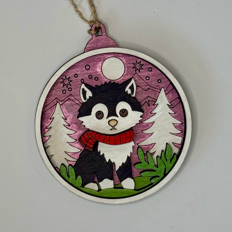 Decorative wooden ornament with a cartoon cat in a scarf against a purple background.