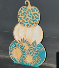 A decorative piece featuring a stacked design of pumpkin and sunflower shapes with a predominantly blue and green color scheme on a wooden surface.