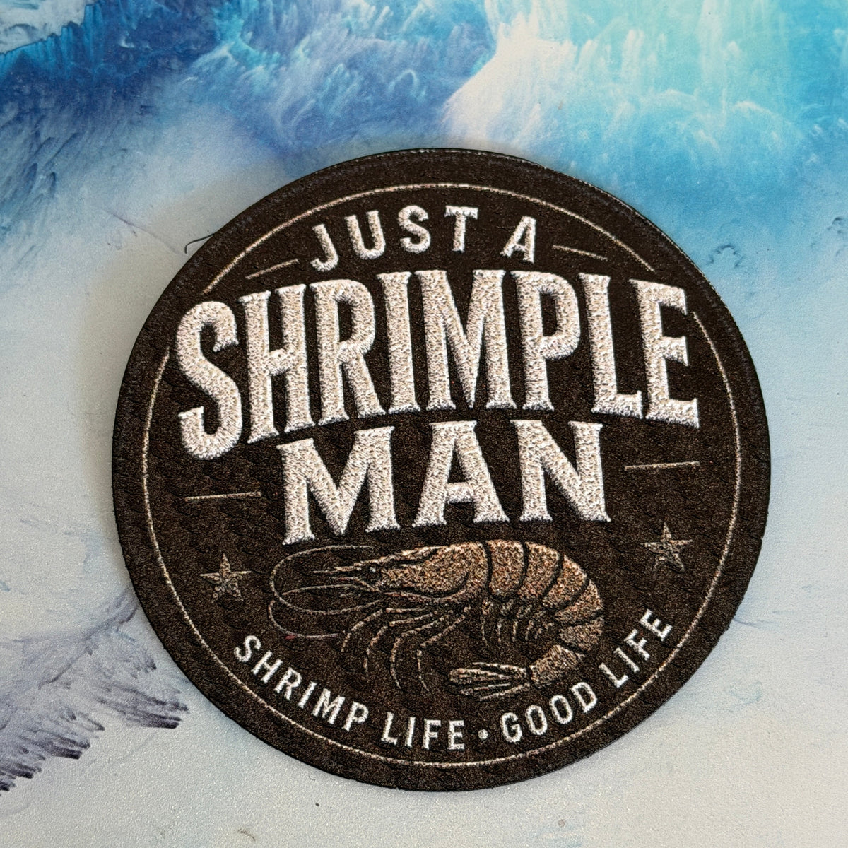 Round sticker with 'Just a Shrimple Man' text and shrimp illustration on a blue and white abstract background