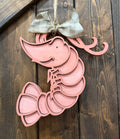 A decorative pink shrimp-shaped hanger with a bow, displayed against a wooden background.