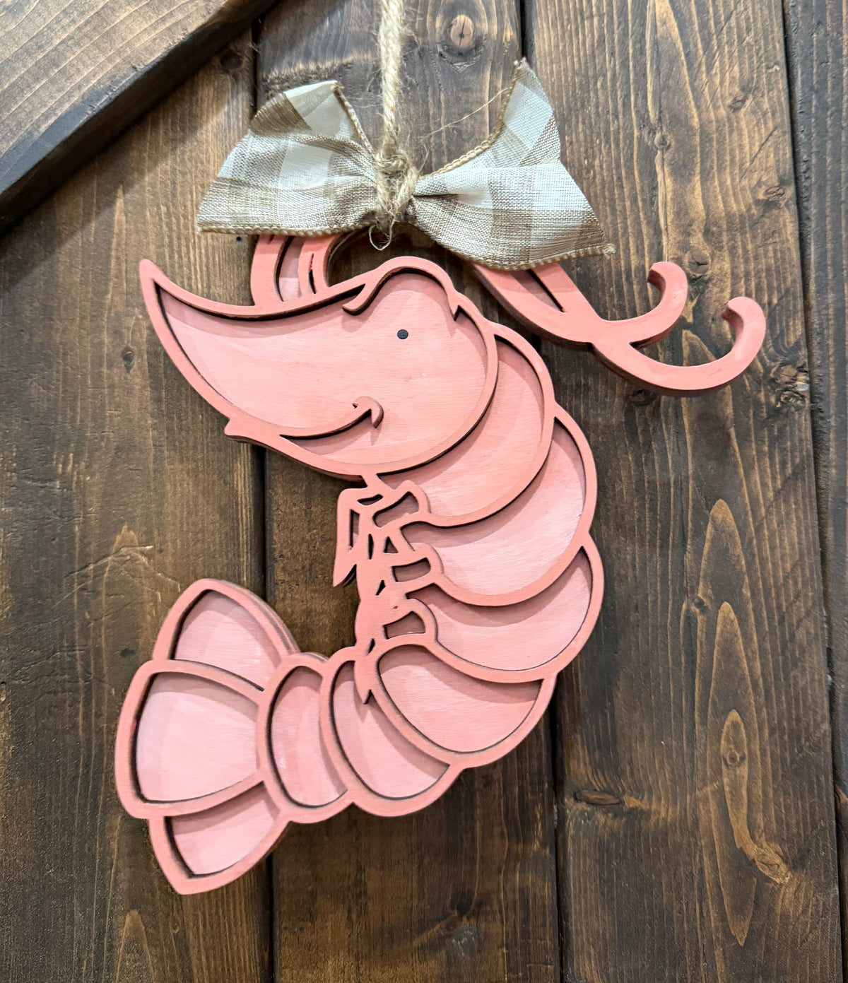 A decorative pink shrimp-shaped hanger with a bow, displayed against a wooden background.