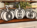 Three white pumpkins with geometric boho patterns laser cut on them, displayed on a wooden surface.