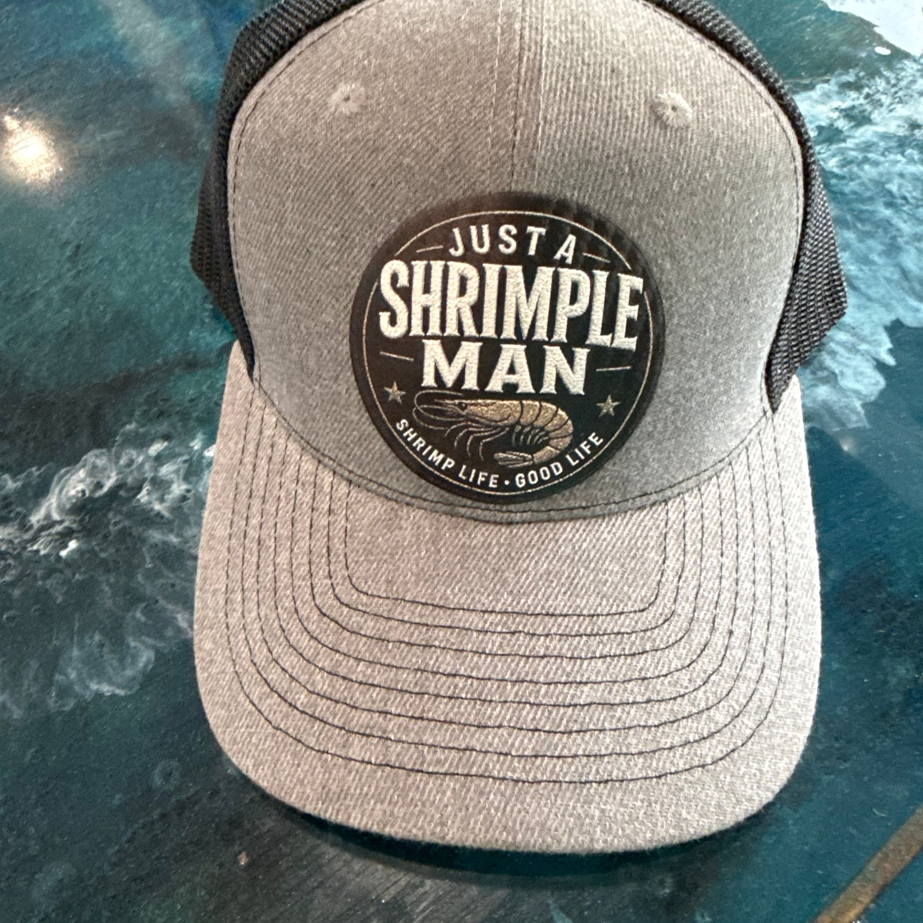 Gray cap with 'Just a Shrimple Man' logo on a reflective surface
