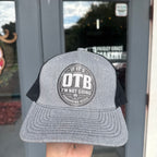 Gray and black cap with 'OTB' logo held in front of a store entrance.