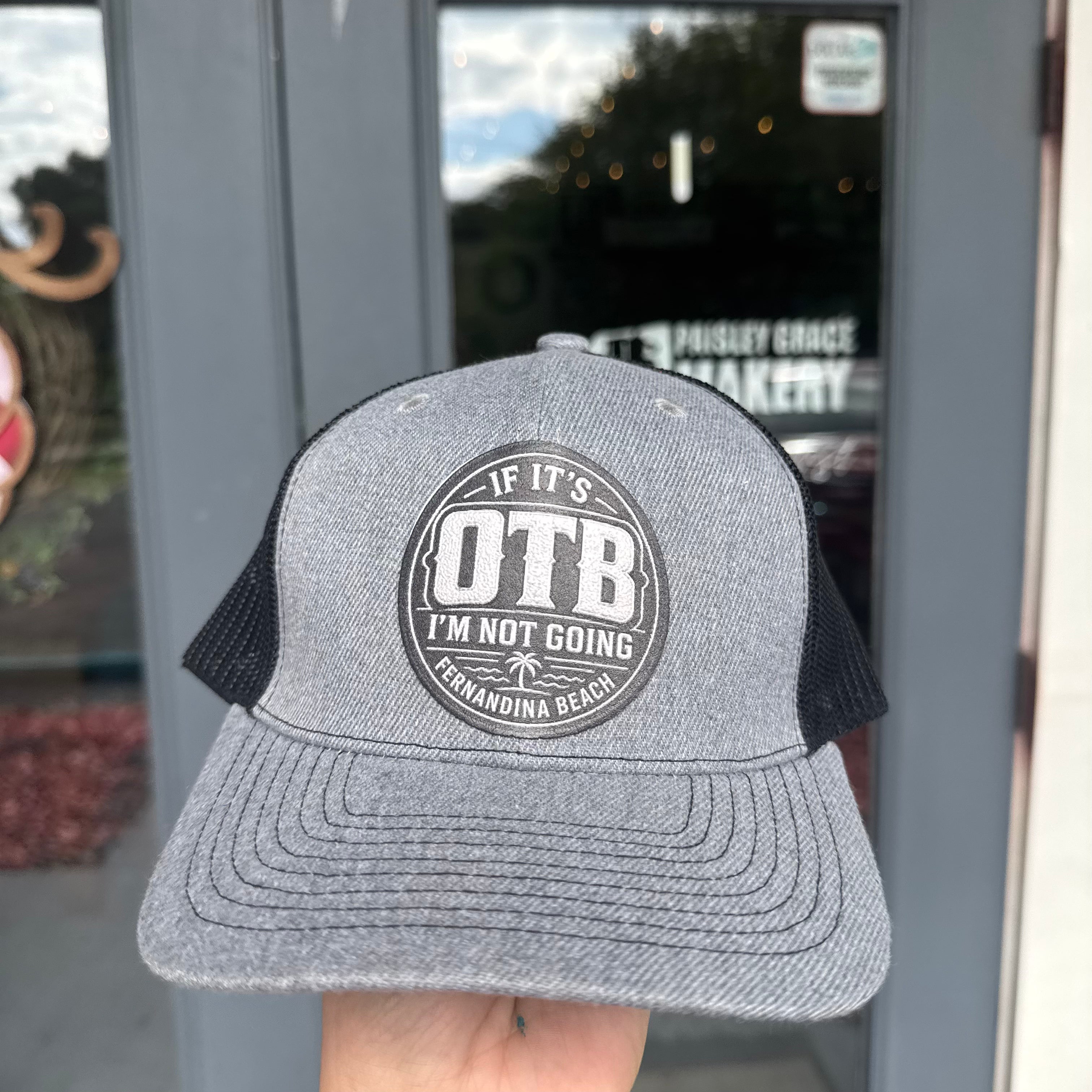 Gray and black cap with 'OTB' logo held in front of a store entrance.