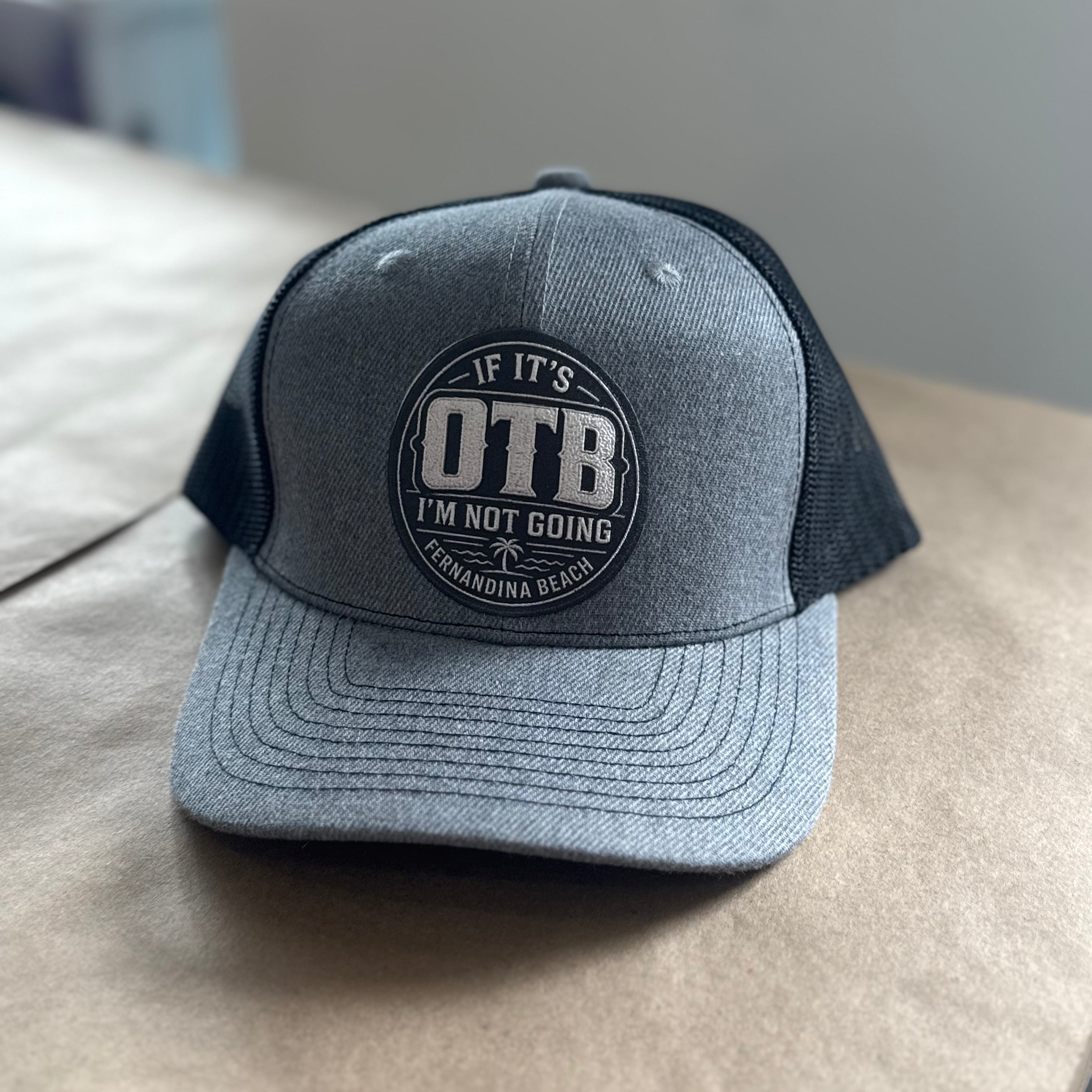 Gray and black cap with 'OTB' logo on a beige surface