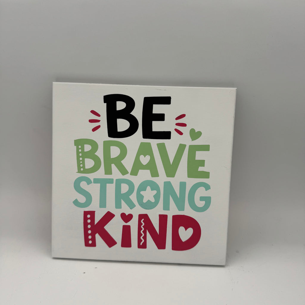 Decorative sign with motivational text 'Be Brave Strong Kind' on a plain background