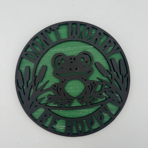 Decorative circular sign with a frog design and text 'Don't Worry Be Happy' on a white background