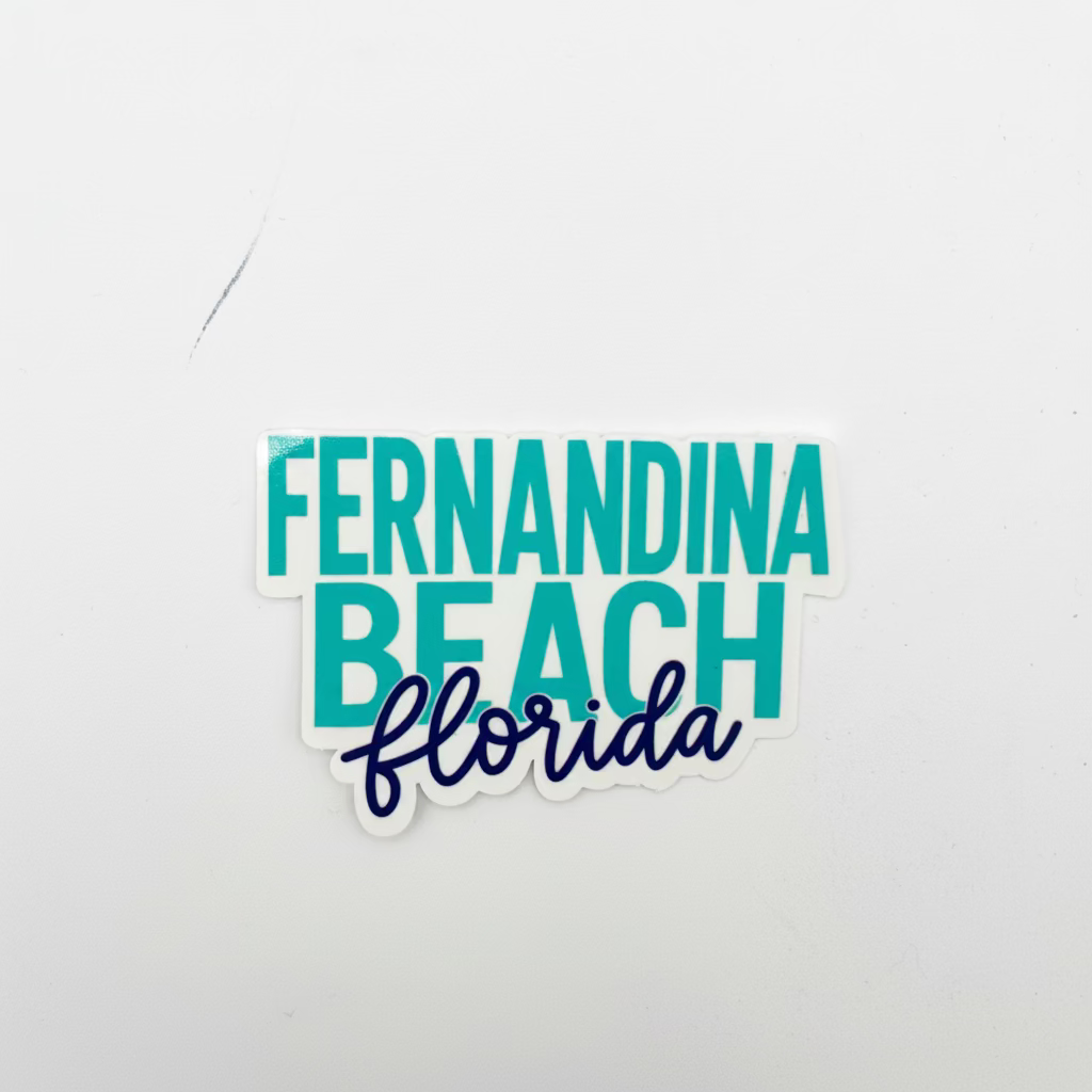 A die-cut sticker reading 'FERNANDINA BEACH florida' on a plain light gray background. The top and middle lines use a teal sans-serif font, while 'florida' is written below in dark navy script.