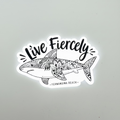 A die-cut sticker featuring a black and white hand-drawn shark with intricate floral mandala patterns, the text 'Live Fiercely' in a stylized font, and 'FERNANDINA BEACH' at the bottom, shown on a plain light gray background.