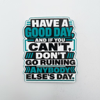 A die-cut vinyl sticker with a motivational quote, displayed on a light gray background. The sticker features a black background with white and teal text reading 'HAVE A GOOD DAY, AND IF YOU CAN'T, DON'T GO RUINING ANYBODY ELSE'S DAY.
