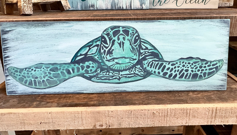 A wall-mounted wooden plank art piece with a turtle design painted in a beachy, watercolor style.